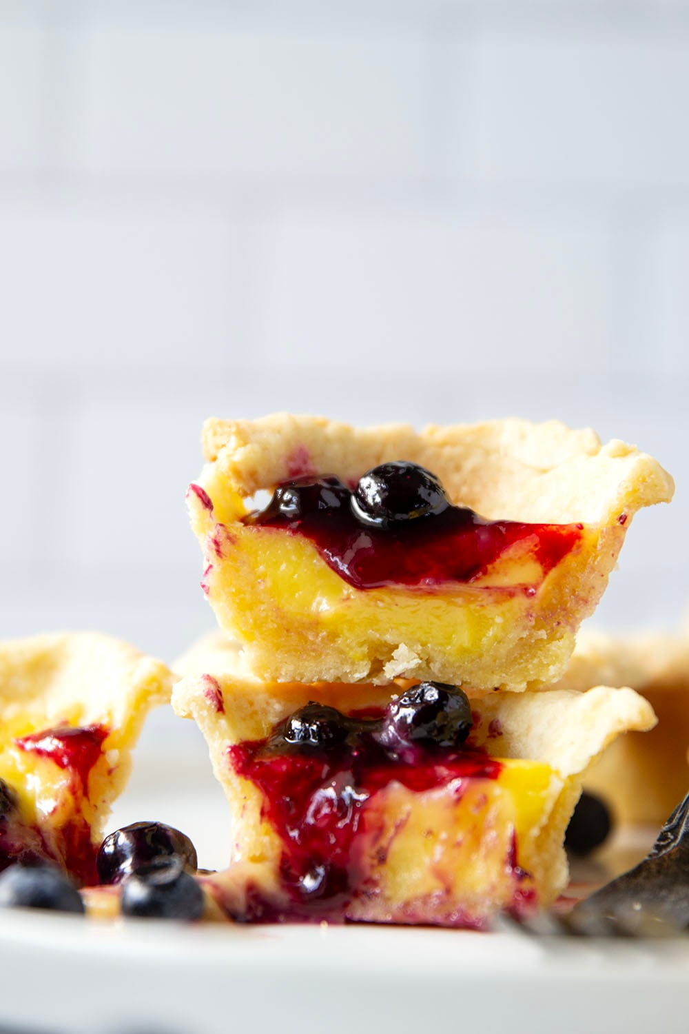 These mini lemon tarts feature a flaky pastry crust, tangy lemon filling, and lots of fresh blueberry sauce spooned on top.