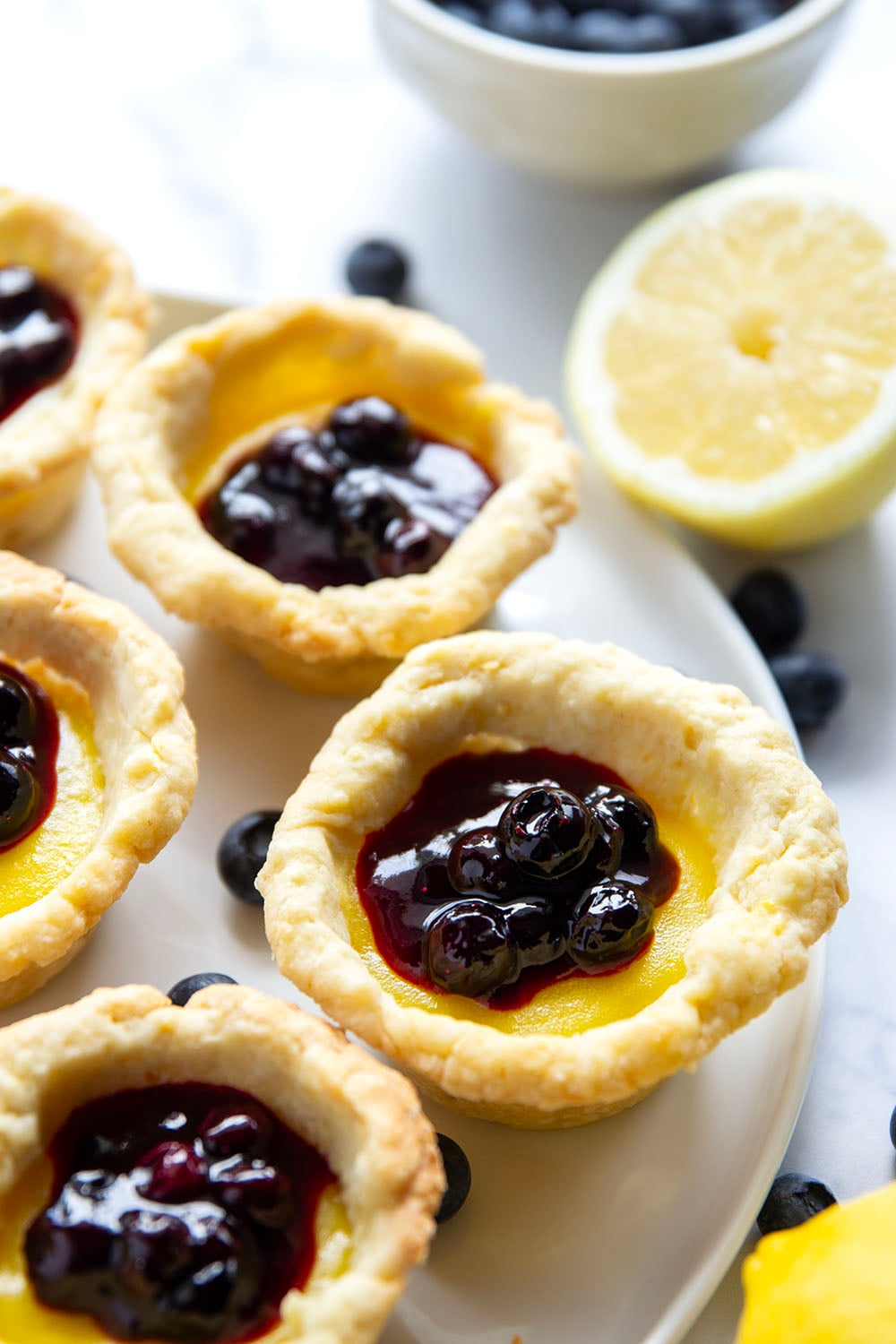 These mini lemon tarts feature a flaky pastry crust, tangy lemon filling, and lots of fresh blueberry sauce spooned on top.