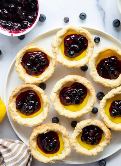 These mini lemon tarts feature a flaky pastry crust, tangy lemon filling, and lots of fresh blueberry sauce spooned on top.