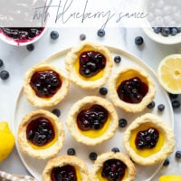 These mini lemon tarts feature a flaky pastry crust, tangy lemon filling, and lots of fresh blueberry sauce spooned on top.