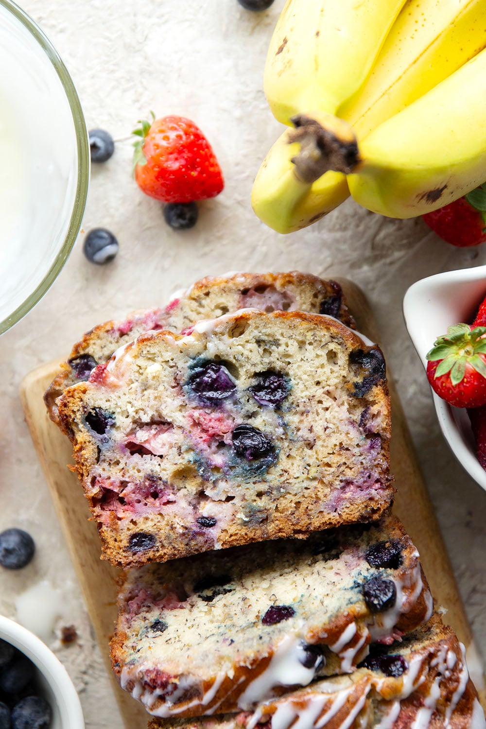 Soft and moist berry banana bread is packed with fresh strawberries, raspberries, and blueberries and topped with a rich cream cheese icing.