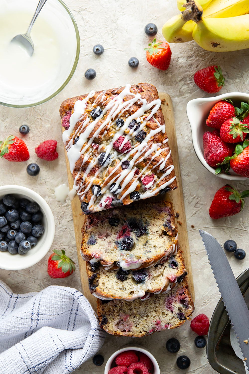 Soft and moist berry banana bread is packed with fresh strawberries, raspberries, and blueberries and topped with a rich cream cheese icing.