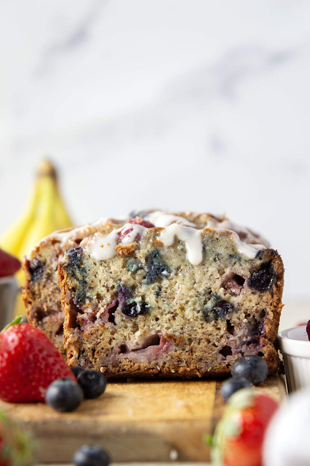 Soft and moist berry banana bread is packed with fresh strawberries, raspberries, and blueberries and topped with a rich cream cheese icing.