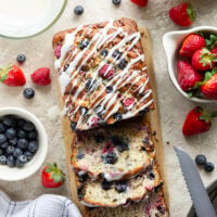Soft and moist berry banana bread is packed with fresh strawberries, raspberries, and blueberries and topped with a rich cream cheese icing.