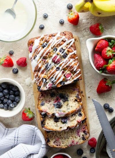 Soft and moist berry banana bread is packed with fresh strawberries, raspberries, and blueberries and topped with a rich cream cheese icing.