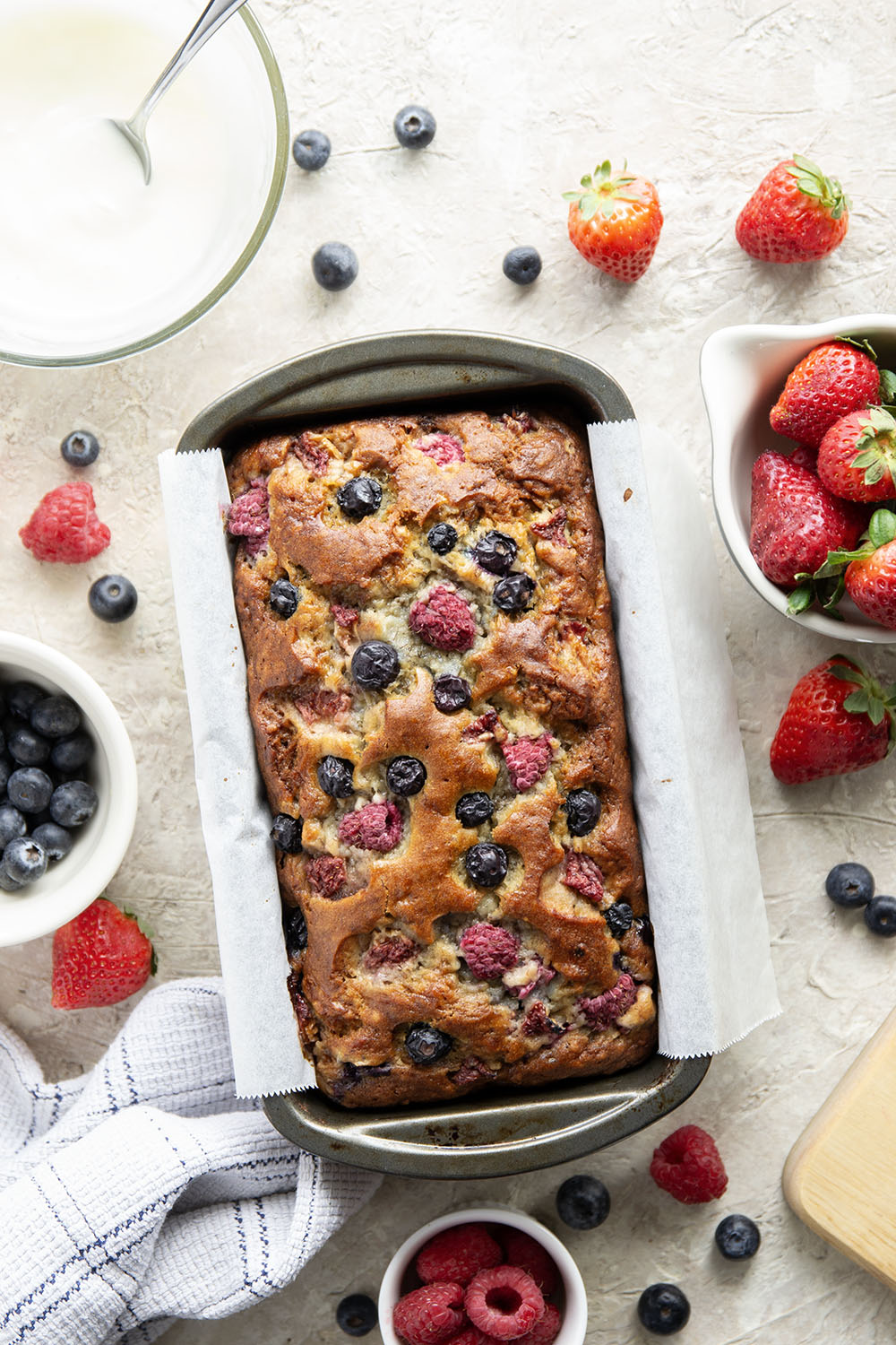Soft and moist berry banana bread is packed with fresh strawberries, raspberries, and blueberries and topped with a rich cream cheese icing.