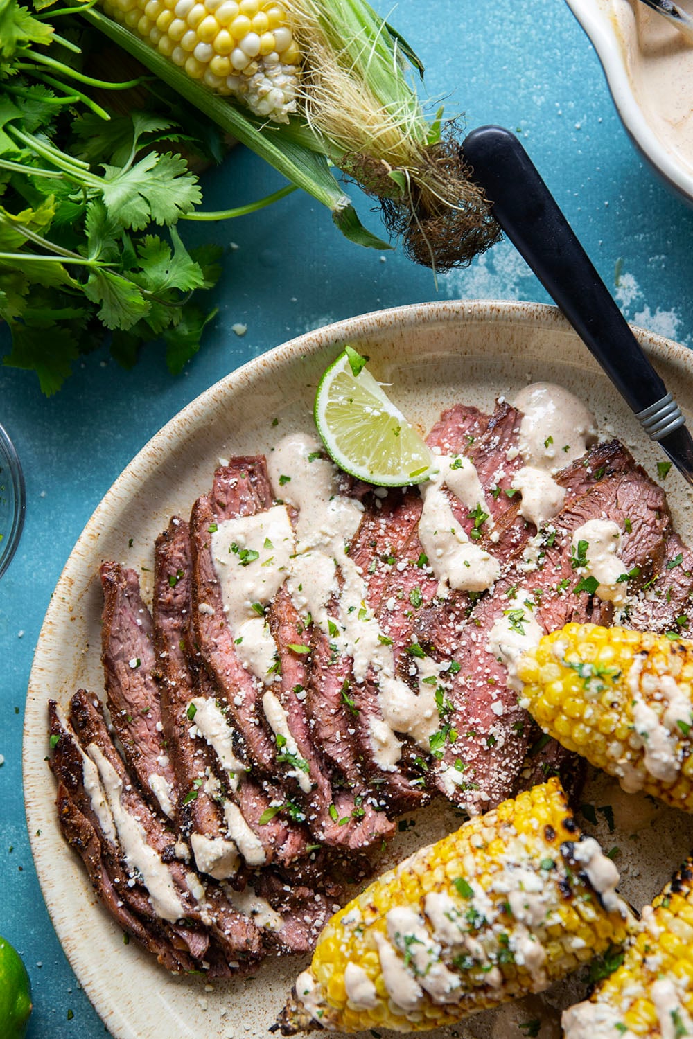 Spice-rubbed grilled flank steak and corn is an easy summer dish that pairs very well with a creamy chili lime sauce drizzled on top.