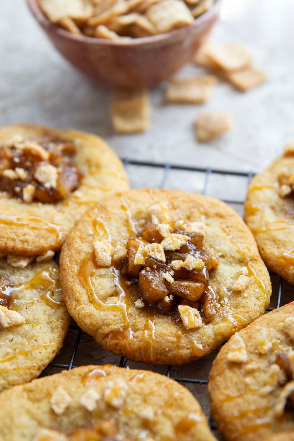 These caramel apple pie cookies feature a soft and chewy butter cookie base with a caramelized apple center, rich drizzles of caramel sauce, and crushed cinnamon crunch cereal on top.