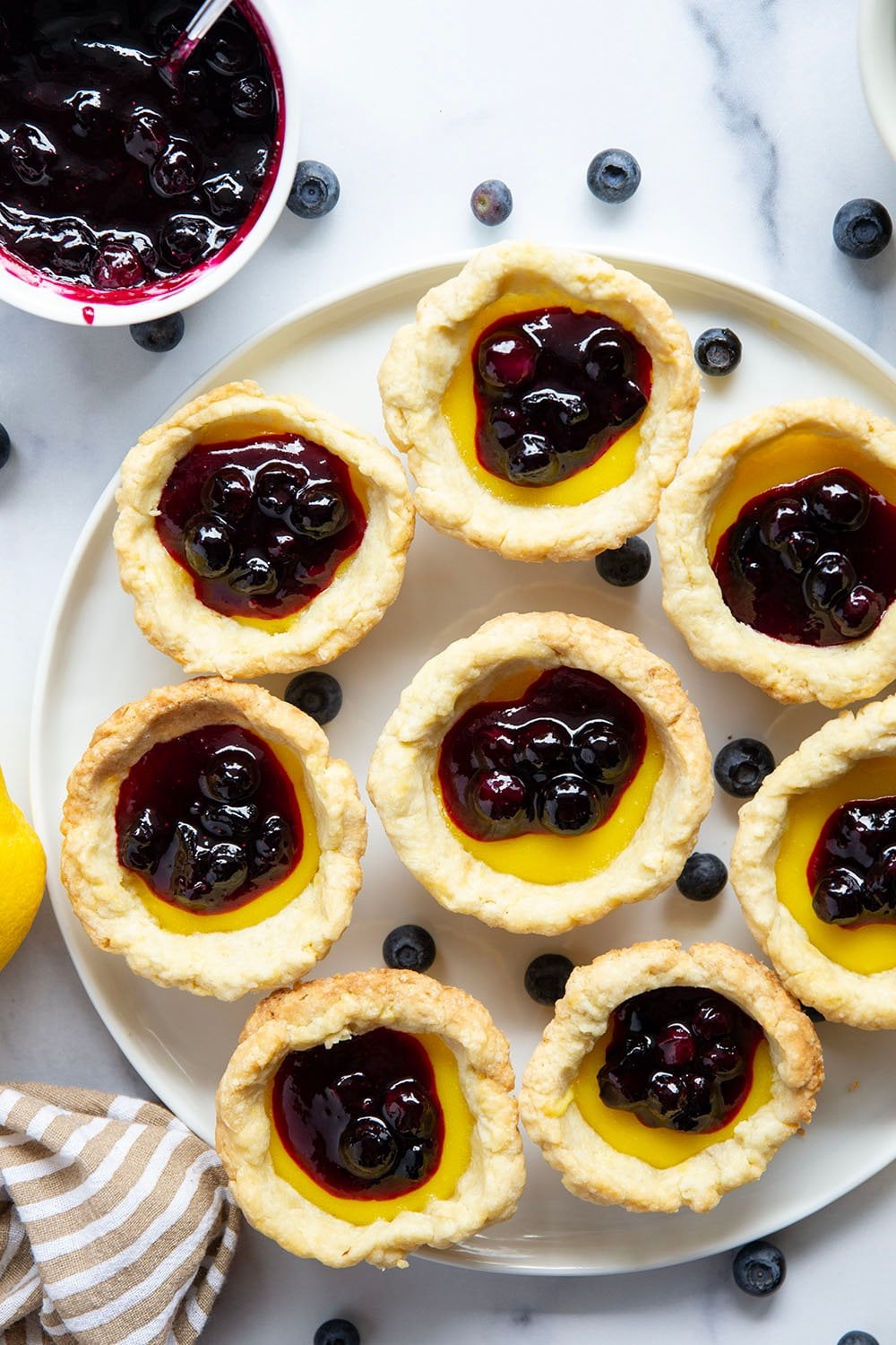 These mini lemon tarts feature a flaky pastry crust, tangy lemon filling, and lots of fresh blueberry sauce spooned on top.
