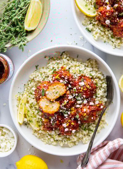 Tender and juicy harissa chicken meatballs are baked in a spicy harissa tomato sauce and served alongside bowls of fluffy lemon herb couscous.