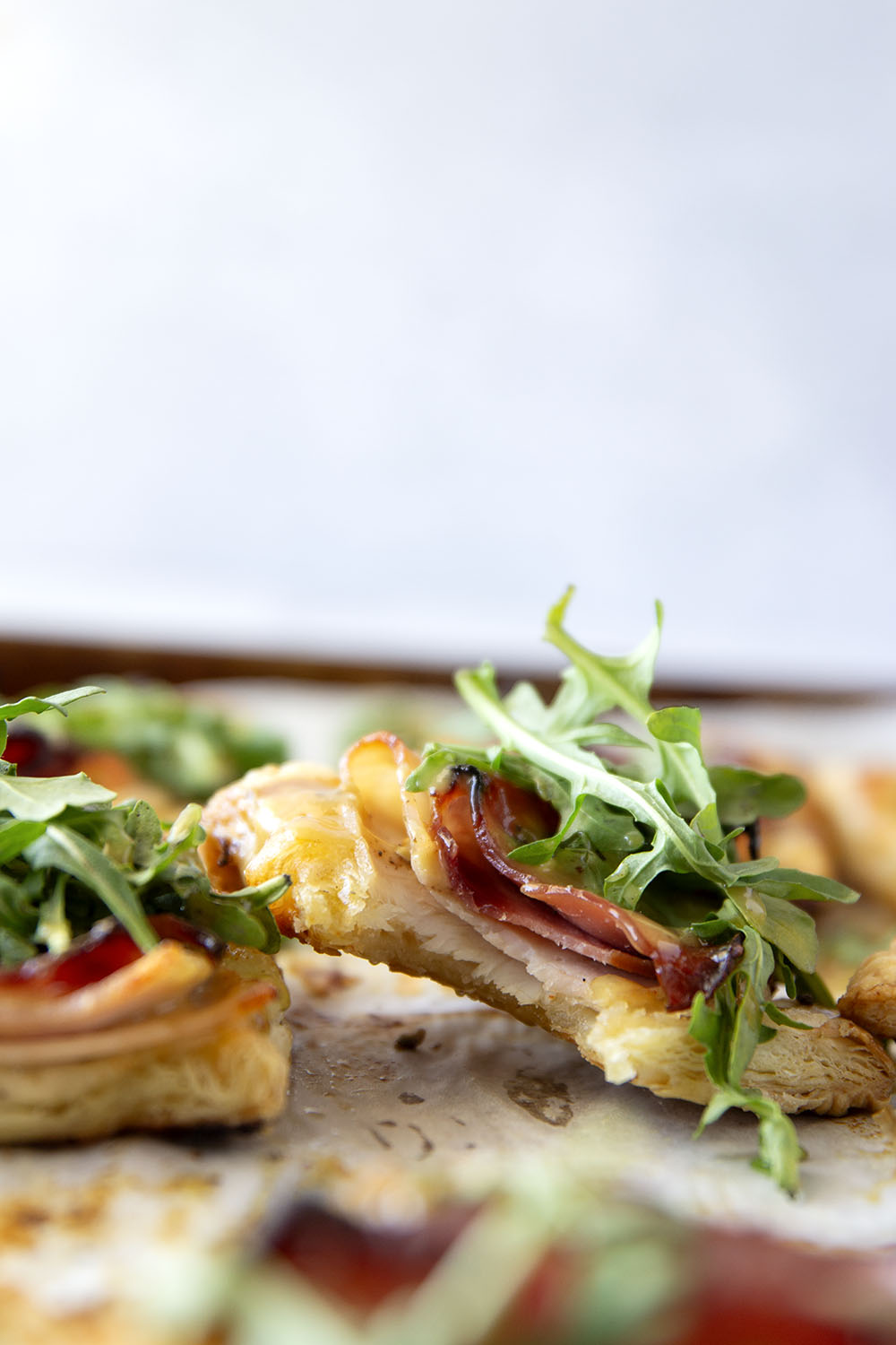 These savory cordon bleu puff pastry tarts have everything you'll find in the classic chicken dish in hand-held tart form! These tarts feature layers of deli ham, chicken, and Swiss cheese slices with a tangy honey mustard and lots of arugula piled on top.