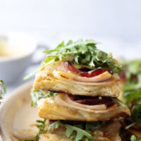 These savory cordon bleu puff pastry tarts have everything you'll find in the classic chicken dish in hand-held tart form! These tarts feature layers of deli ham, chicken, and Swiss cheese slices with a tangy honey mustard and lots of arugula piled on top.