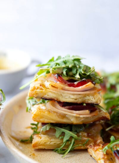 These savory cordon bleu puff pastry tarts have everything you'll find in the classic chicken dish in hand-held tart form! These tarts feature layers of deli ham, chicken, and Swiss cheese slices with a tangy honey mustard and lots of arugula piled on top.