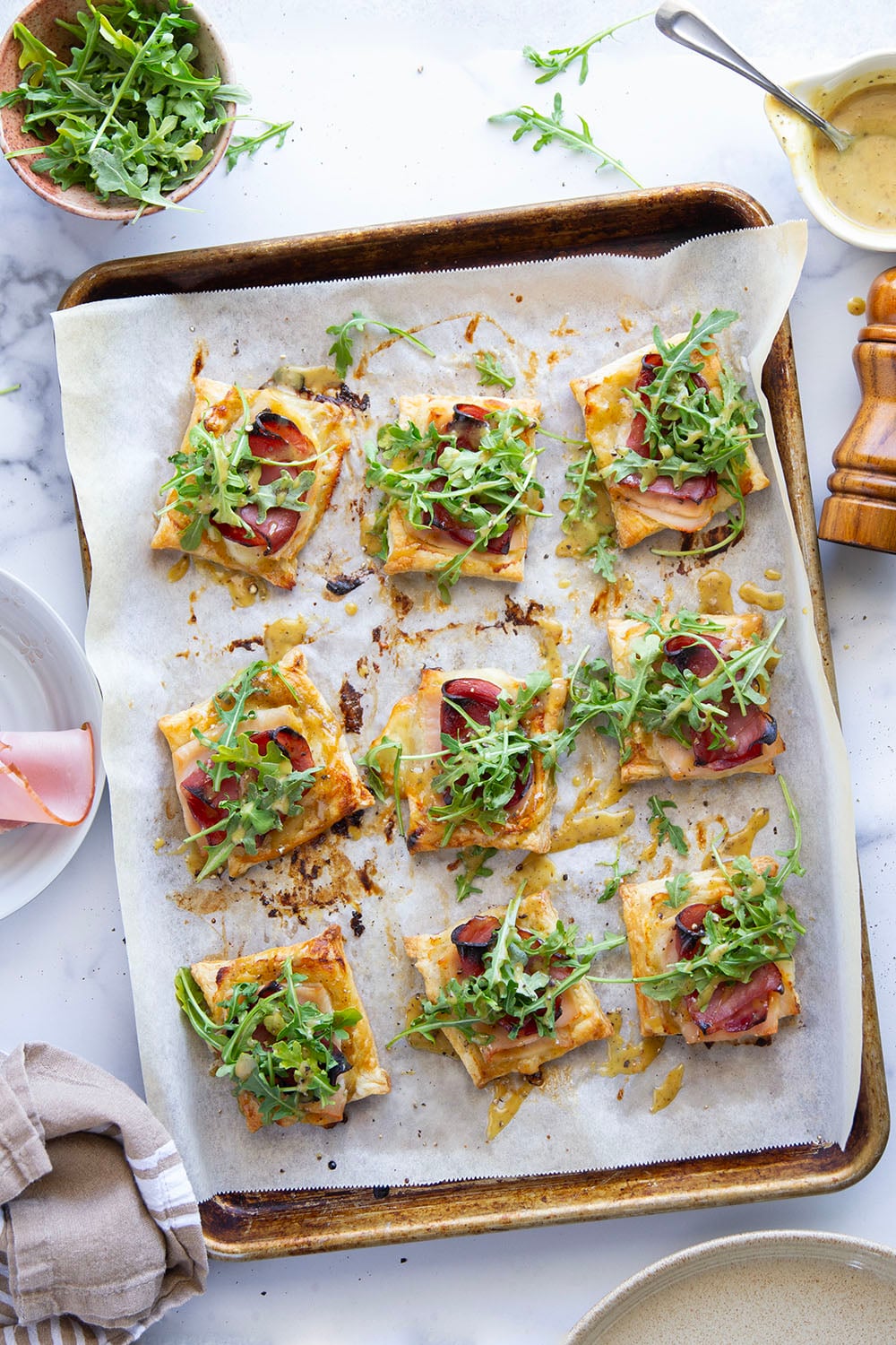 These savory cordon bleu puff pastry tarts have everything you'll find in the classic chicken dish in hand-held tart form! These tarts feature layers of deli ham, chicken, and Swiss cheese slices with a tangy honey mustard and lots of arugula piled on top.