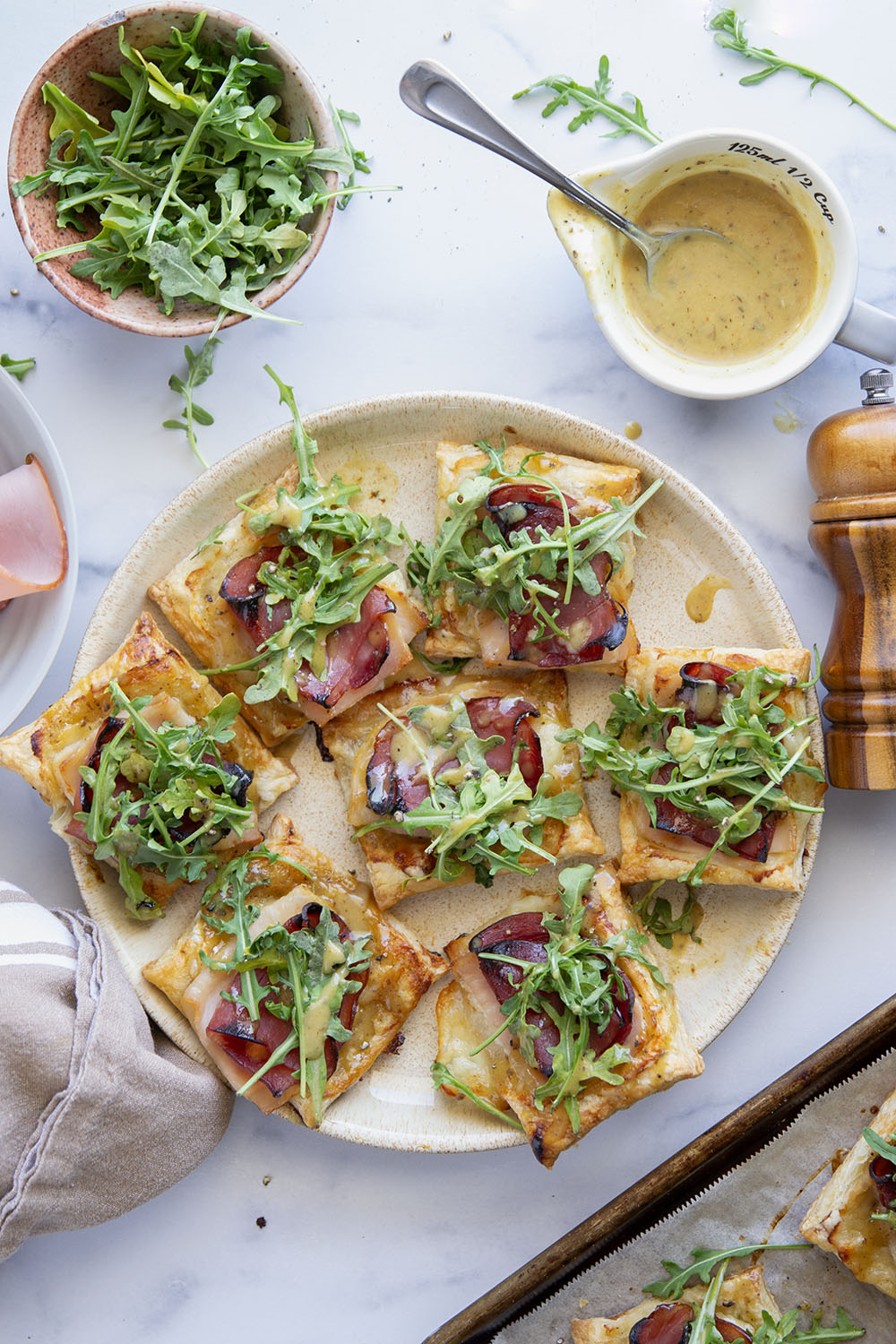 These savory cordon bleu puff pastry tarts have everything you'll find in the classic chicken dish in hand-held tart form! These tarts feature layers of deli ham, chicken, and Swiss cheese slices with a tangy honey mustard and lots of arugula piled on top.