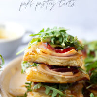 These savory cordon bleu puff pastry tarts have everything you'll find in the classic chicken dish in hand-held tart form! These tarts feature layers of deli ham, chicken, and Swiss cheese slices with a tangy honey mustard and lots of arugula piled on top.