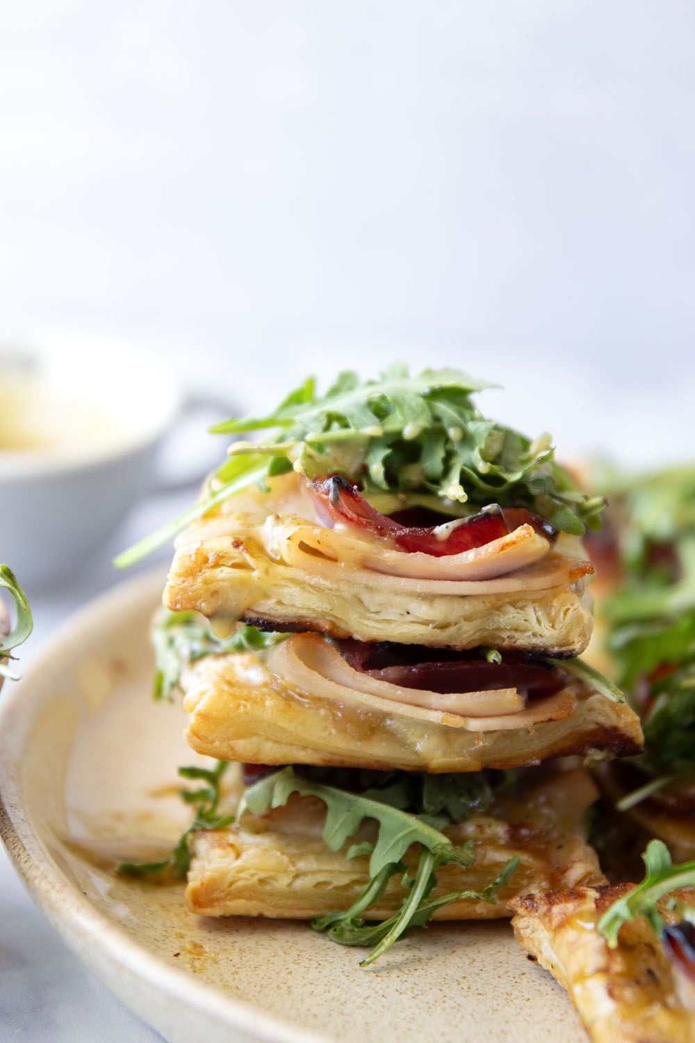 These savory cordon bleu puff pastry tarts have everything you'll find in the classic chicken dish in hand-held tart form! These tarts feature layers of deli ham, chicken, and Swiss cheese slices with a tangy honey mustard and lots of arugula piled on top.