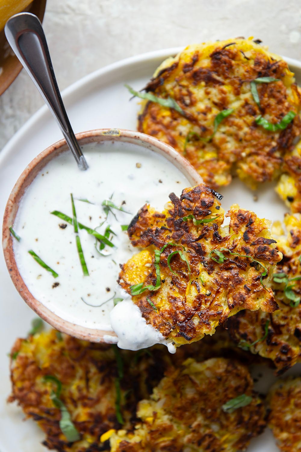 These yellow squash fritters feature perfectly crispy exteriors with a moist, flavorful texture inside. Serve them hot and crispy from the skillet with an herby fresh basil sour cream.